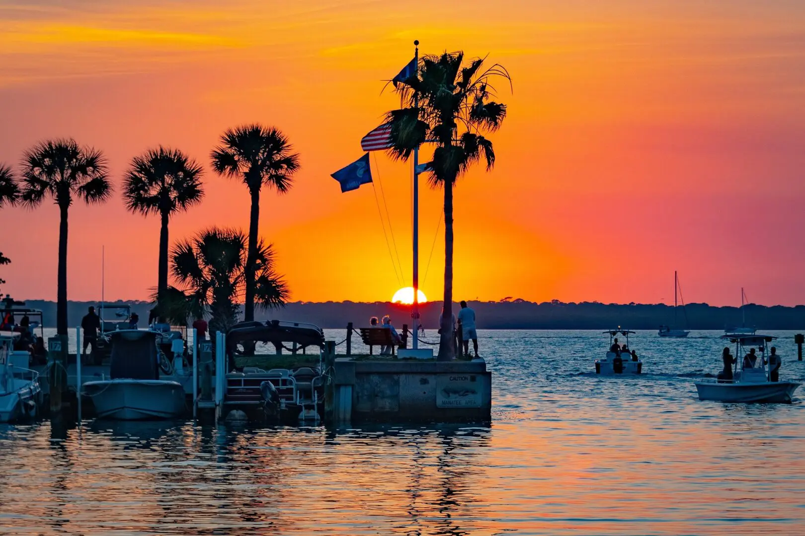 A sunset over the water with palm trees and boats.